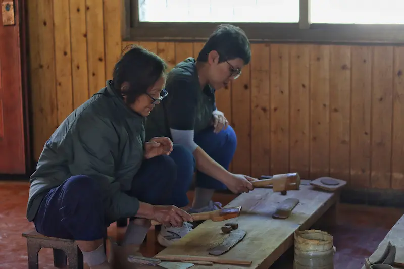 Two Singaporean guests shaping black pottery cups with a wooden tool.