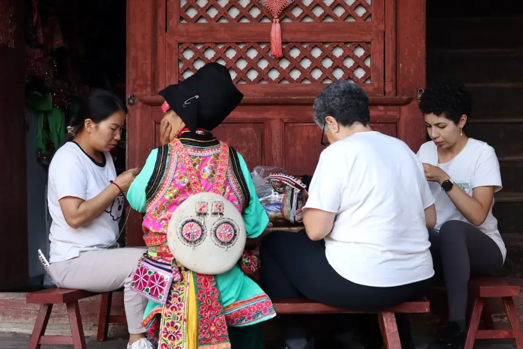 Two guests doing traditional embroidery work with a local Yi woman.