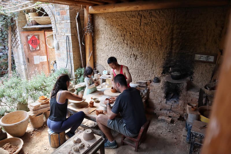 Visitors trying traditional pottery-making with a local craftsman in 600-year-old Jingtian Village, Dali, Yunnan.