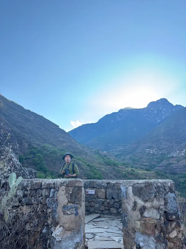 Vistor standing on a stone lookout overlooking mountains and the valley near Shitou Stone Village, Lijiang, Yunnan
