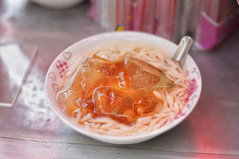 Weishan jelly drink with shrimp-shaped rice noodles and brown sugar syrup, a traditional Yunnan snack.