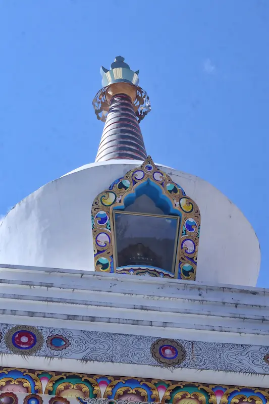 White Tibetan Buddhist stupa with golden spire and ornate painted decorations against blue sky in Yunnan.
