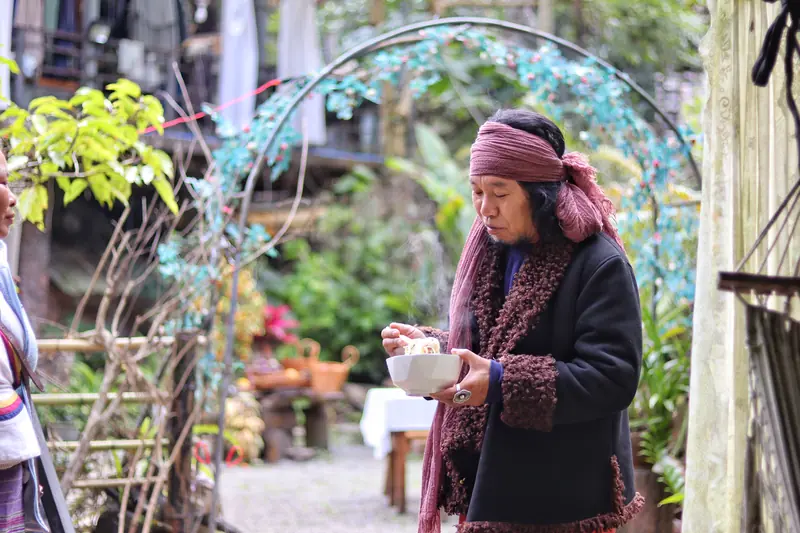 Aini (Hani) man in traditional dress holding a bowl of food in his village, Xishuangbanna