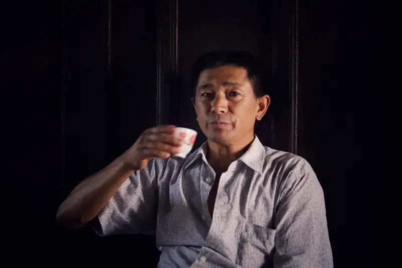 A man enjoying a cup of tea in the dim, traditional interior of a Baoshan tea shop