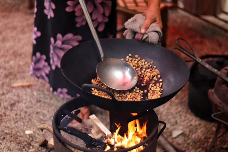 Roasting coffee beans in a wok over a fire during a traditional Dai coffee experience