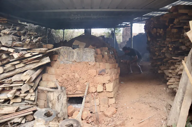 Stacked firewood beside a traditional dragon kiln in a pottery village near Ning'er
