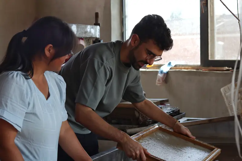Visitors trying hands-on traditional papermaking at the screen with a local family