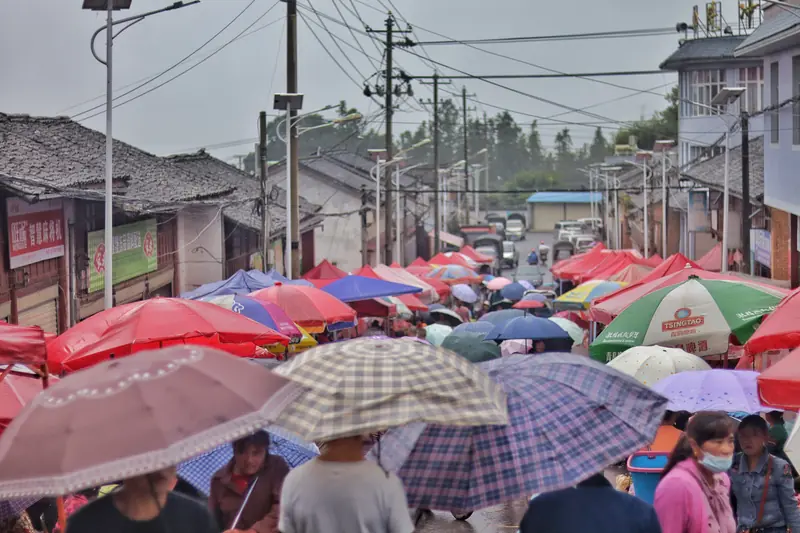 Crowds shopping under colorful umbrellas at a lively Tengchong ethnic farmers' market