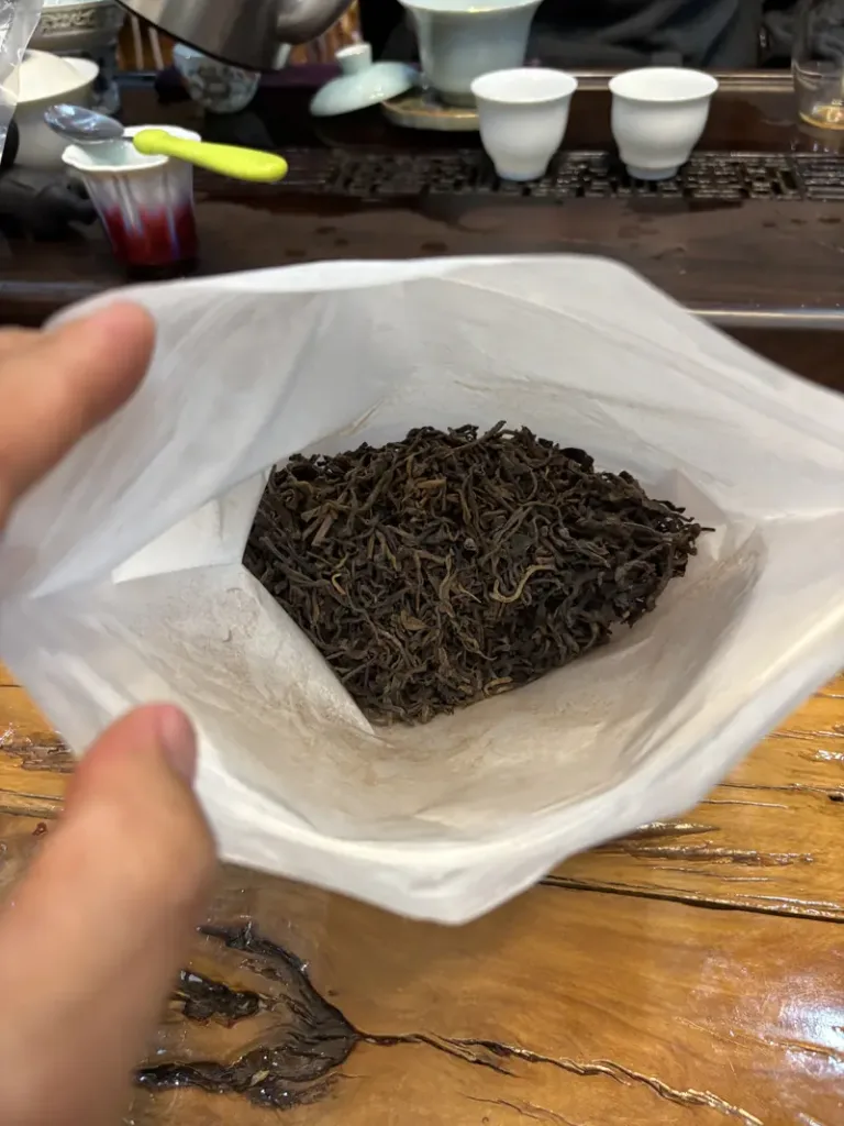 Hand holding dried Pu-erh tea leaves at a tea family's home in Yiwu