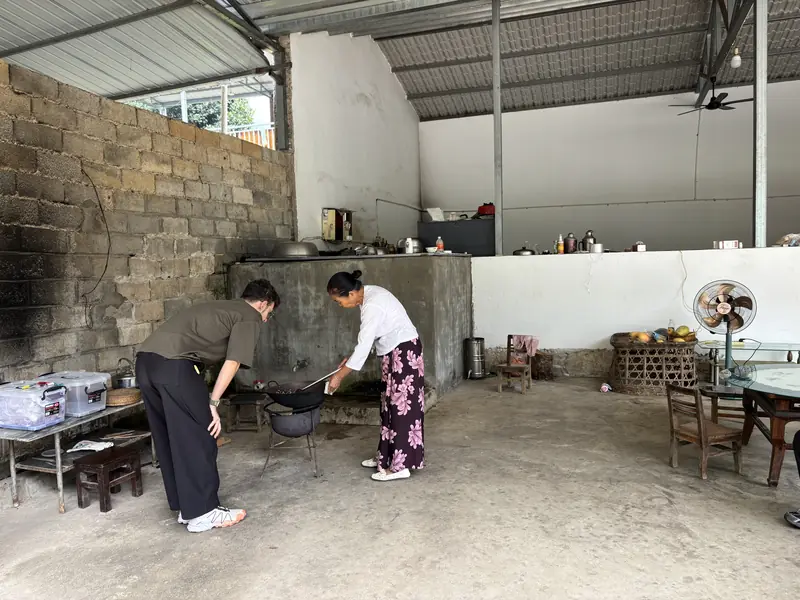 Dai village woman teaching a visitor to roast coffee beans in a wok at a Yunnan Arabica farm