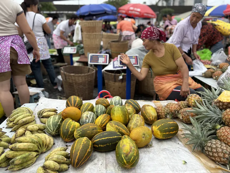 A market stall piled with fresh melons and pineapples at a Yunnan ethnic market
