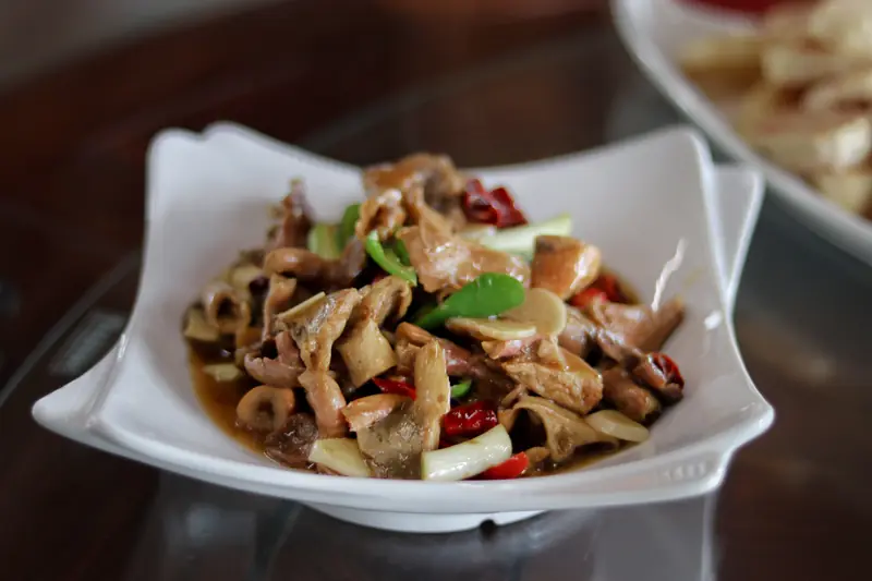 Stir-fried wild mushrooms with green peppers and chili in a white bowl at a Yunnan meal