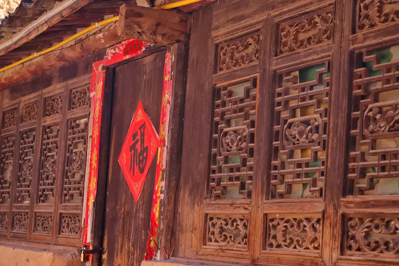 A traditional Chinese wooden house with red couplets at the entrance and a large red “福” character in the center symbolizing happiness.