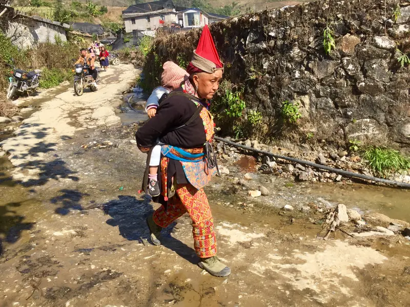 A woman in traditional dress carries a child along a village path in Yunnan.
