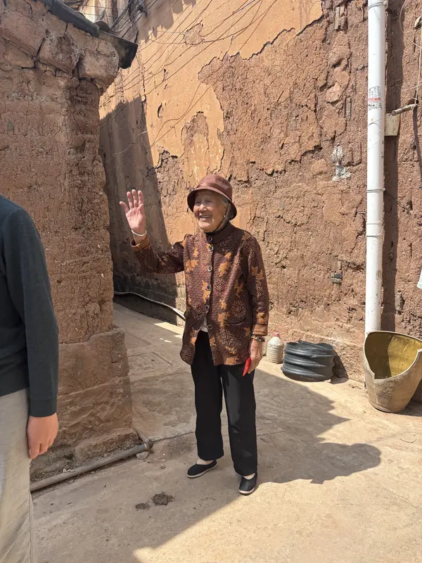 An elderly resident waves from a brick alley in the Tonghai village visited for its foot-binding history.