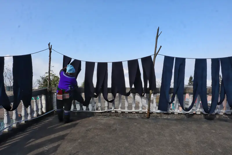 A Yi woman hangs indigo-dyed cloth, continuing a traditional dyeing practice.