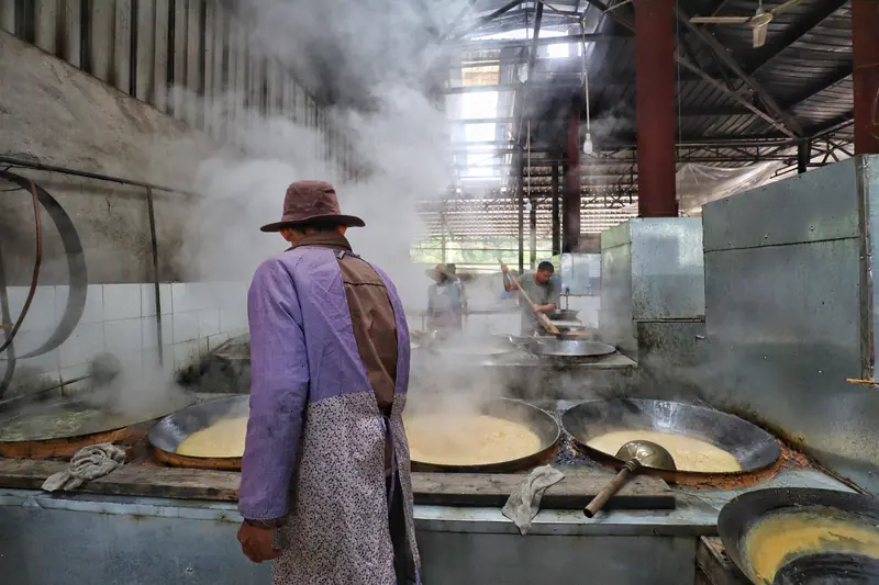 A visitor watches cane sugar being boiled in steaming pans at a traditional workshop.