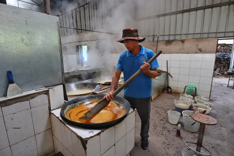 A worker stirs cane sugar over a wok using traditional methods.