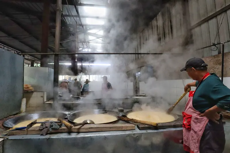 A worker stirs boiling cane sugar juice over a wood-fired wok.