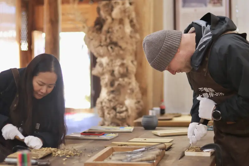 Visitor trying hands-on wood carving with a local artisan, Yunnan